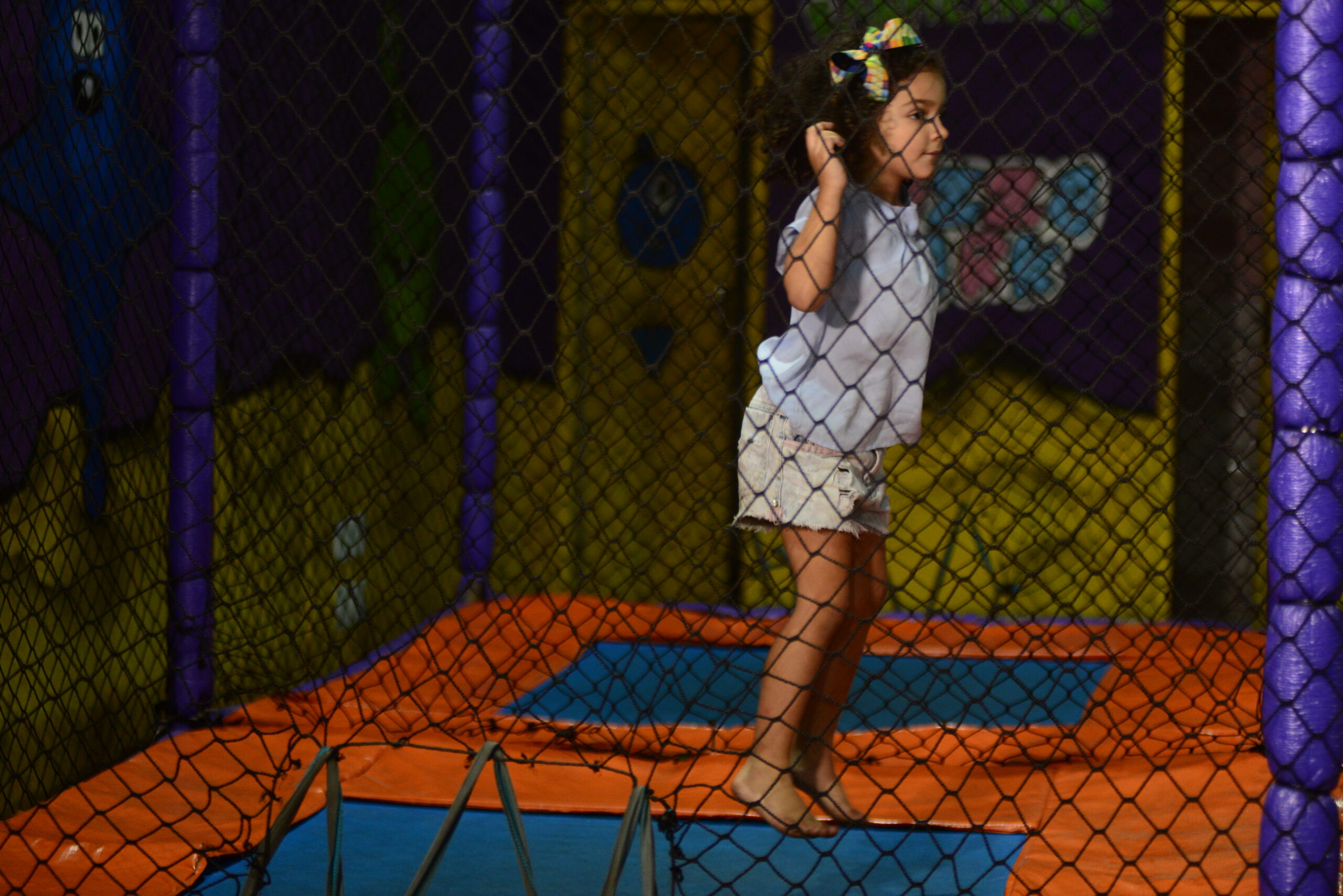 Menina pula em cama elástica toda cercada por tela de proteção.